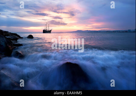 Ein Piratenschiff Segel entlang des Ozeans bei Sonnenuntergang, wie die Wellen in Ufer. Stockfoto
