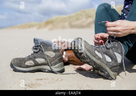 Junge Frau ihre Wanderschuhe ausziehen, am Strand von Harlech. Stockfoto