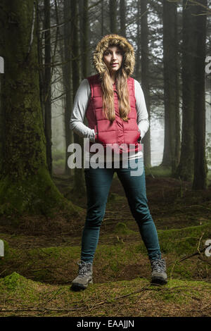 Eine junge Frau in einem Wald mit ihre Hände in den Taschen und Kapuze oben stehend. Stockfoto