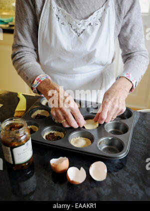 Ältere Frau Rentner Mince Pies zu Hause in ihrer Küche zu Weihnachten backen. Setzen das Hackfleisch in die Gebäck-Schalen Stockfoto