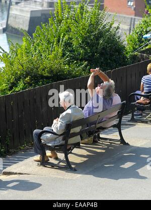 Ein Mann mit seinen Händen um seine Augen vor der Sonne zu schützen, sitzend auf einer Bank, Padstow, Cornwall England uk Stockfoto