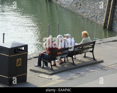 vier Leute sitzen auf einer Bank im Hafen von Padstow, Cornwall, England uk Stockfoto