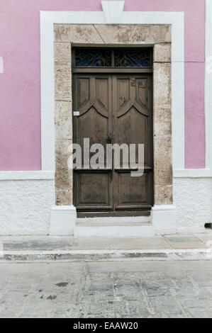 Nahaufnahme eines großen braunen Holztür mit Stein Türverkleidungen auf einem rosafarbenen und weißen Stuck spanische Kolonialgebäude, Campeche, Mexiko Stockfoto