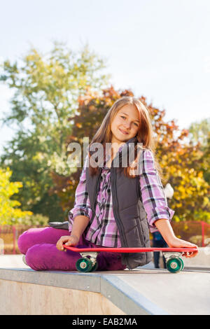 Positive Mädchen hält es Skateboard sitzt auf Boden Stockfoto