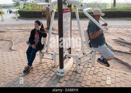 In einer anderen Übung, Kontrast von Frau auf Handy und Mann stretching auf Übung Maschinen in Vientiane, der Hauptstadt von Laos, Südostasien, Asien, Stockfoto