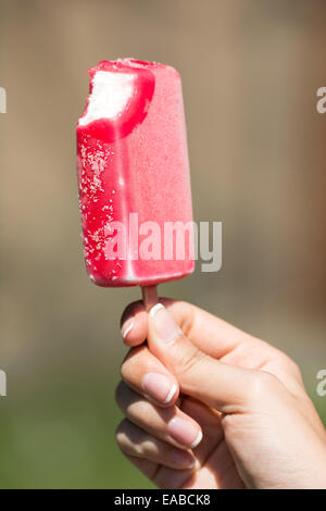 Mädchen-Hand mit Rosa Eis auf Stick gebissen Stockfoto