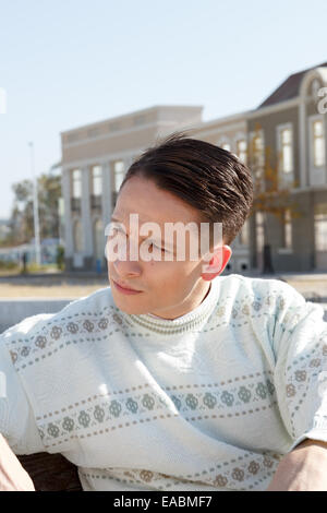 gut aussehender Mann posiert in weißen Pullover und Standortwahl auf Bank in der Stadt und auf der Suche zur Seite Stockfoto