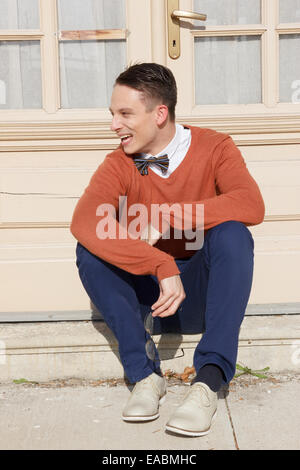 glücklich Jüngling in Pullover sitzen auf Stufen vor der Haus und posiert, Vintage retro-Foto Stockfoto