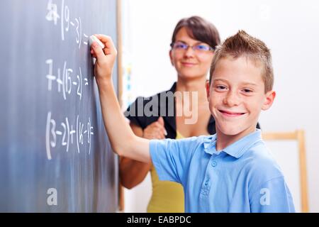 Fröhliche junge vor der Tafel steht. Lehrer steht hinter Stockfoto