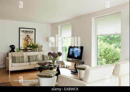Großen weißen Knöpfen Sofa mit gestreiften Kissen im Wohnzimmer mit gerahmten Vintage Poster, Flatscreen-TV und große Fenster