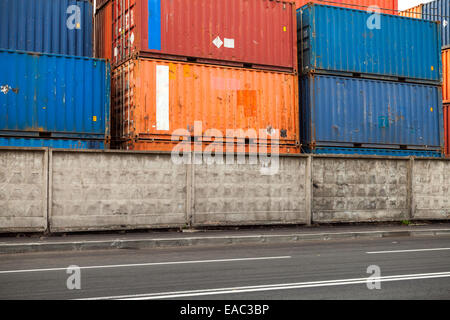 Industrielle Frachtcontainer sind im Hafengebiet hinter alten Betonzaun gestapelt. Stockfoto