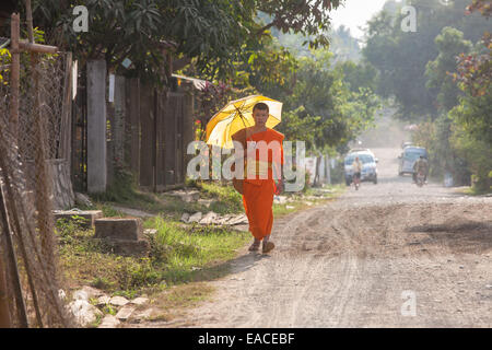 Buddhistischer Mönch mit Regenschirm zu Fuß durch Ban Xang Khong Dorf in der Nähe von Luang Prabang, Laos, Südostasien, Asien, Stockfoto