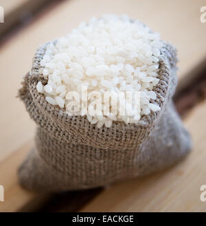 Reis in einem Leinensack auf hölzernen Hintergrund Stockfoto