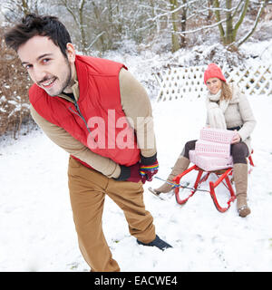 Glückliches Paar Rodeln im Winter mit Schlitten mit Weihnachtsgeschenken Stockfoto