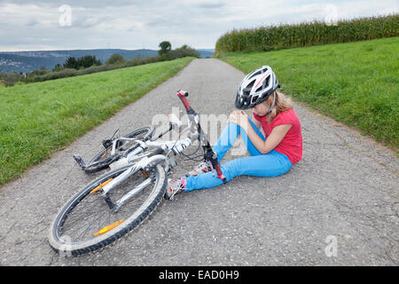 Mädchen, 9 Jahre, das Tragen eines Helms beim Radfahren, halten ihr Knie nach einem Sturz mit dem Fahrrad Stockfoto