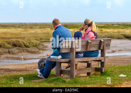 Familie, Essen zum mitnehmen auf einer Bank am Moreston Quay, Norfolk, Großbritannien Stockfoto