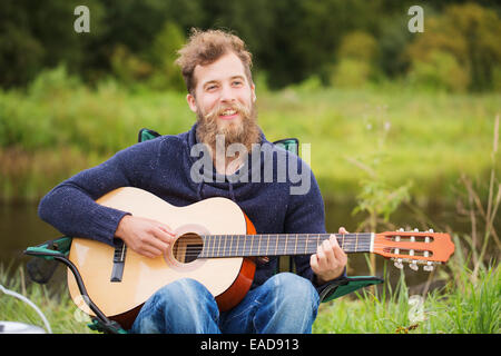 lächelnder Mann spielt Gitarre in camping Stockfoto