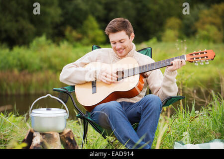 lächelnder Mann mit Gitarre und Dixie im camping Stockfoto