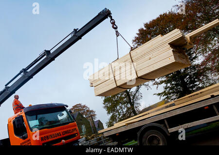 Ausfahrbare Kran verwendet wird, um die hölzerne Planken von der Rückseite eines LKW auf einer Baustelle zu heben Stockfoto