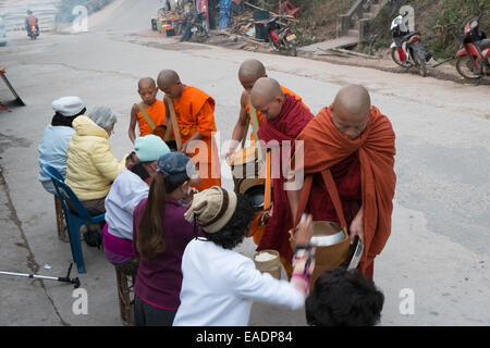 Buddhistische Mönche gehen sehr früh Almosen mit Bettelschalen, um Almosen zu empfangen, Essen von Anhängern, Pakbeng Dorf, Mekong Fluss, Laos, Asien. Stockfoto