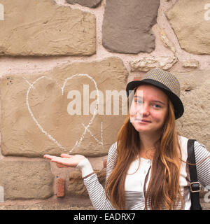 Junge Mädchen in der Nähe einer Wand gemalt Kreide Herz und Pfeil. Stockfoto