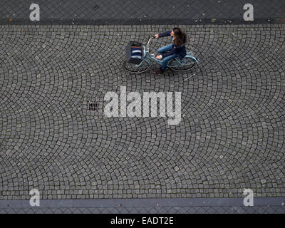 Draufsicht auf eine junge Frau mit dem Fahrrad auf einer gepflasterten Straße Stockfoto