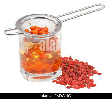 Kochen der Goji-Beere Tinktur - Sieb in Glas mit Goji-Beeren-Infusion und Handvoll getrockneten Früchten isoliert auf weißem Rücken Stockfoto