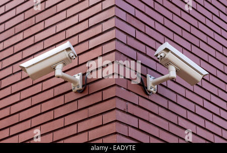 Zwei Überwachungskameras auf dem Brick Wand mit Blick auf gegenüberliegenden Seiten Stockfoto