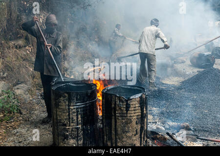 Ein Arbeiter Heizung Teer in Fässern mit offenem Feuer auf einer Straßenbaustelle, Shimla, Himachal Pradesh, Indien Stockfoto