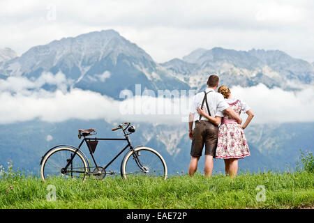 Mann und Frau tragen Tracht mit einem alten Fahrrad mit Blick auf die Berge, Aldrans, Tirol, Österreich Stockfoto