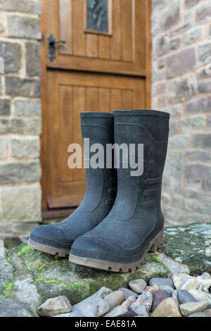 Ein paar schwarze Gummistiefel vor der Tür eines Hauses. Stockfoto