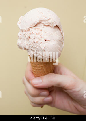 Hand, die eine Kugel Erdbeereis im Waffelhörnchen Stockfoto