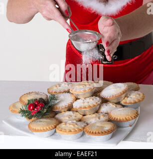 Frau im Santa Outfit setzt Puderzucker Richtfest auf Mince Pies eine traditionelle Weihnachtszeit behandeln Stockfoto