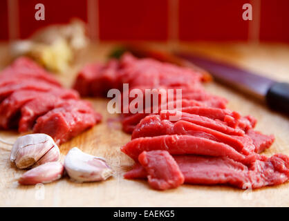 geschnittene Streifen von frischem rosa rohes Rumpsteak mit Knoblauch Zwiebeln auf einem hölzernen chopping Board differenzielle Fokus Stockfoto