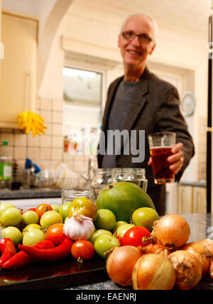 Ein Mann in einer Küche genießen Sie einen Pint Bier - der Fokus ist auf die Zutaten, die er benutzen wird, um ein Chutney zu machen Stockfoto