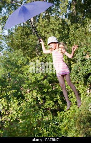 kleines Mädchen mit blauen Schirm oben Sommer Garten Bäume fliegen Stockfoto