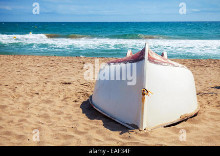 Altes weißes Boot legt sich Hals über Kopf auf dem sandigen Strand der Mittelmeerküste Stockfoto