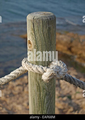 Verknoteten Seil um Holzmaserung Pfahl neben felsigen Meer Ledge Stockfoto