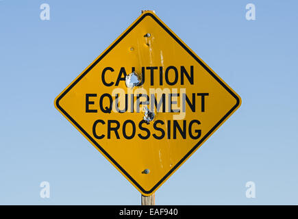 Vorsicht-Ausrüstung überqueren Straßenschild mit Einschusslöchern Stockfoto