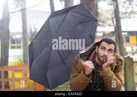 Mann hält Regenschirm und sitzen auf einer Bank Stockfoto