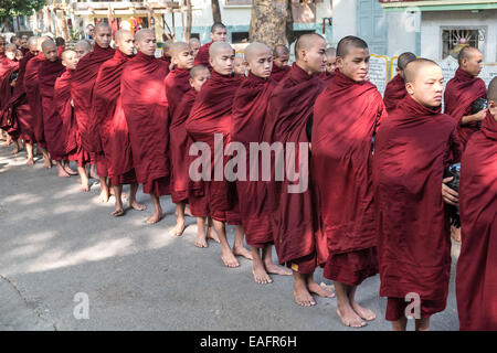 Barfüßige buddhistische Mönche stehen für ihr Mittagessen an, von Gegenständen, die Almosen erhalten, von Almosen, die im Maha Ganayon Kyaung Kloster, Mandalay, geben Stockfoto