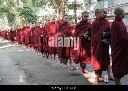 Barfüßige buddhistische Mönche stehen für ihr Mittagessen an, von Gegenständen, die Almosen erhalten, von Almosen, die im Maha Ganayon Kyaung Kloster, Mandalay, geben Stockfoto