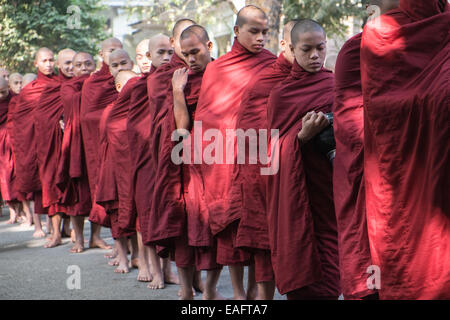 Barfüßige buddhistische Mönche stehen für ihr Mittagessen an, von Gegenständen, die Almosen erhalten, von Almosen, die im Maha Ganayon Kyaung Kloster, Mandalay, geben Stockfoto