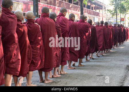 Barfüßige buddhistische Mönche stehen für ihr Mittagessen an, von Gegenständen, die Almosen erhalten, von Almosen, die im Maha Ganayon Kyaung Kloster, Mandalay, geben Stockfoto