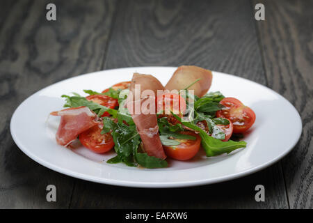 Salat mit Schinken, Rucola und Tomaten, auf Holztisch Stockfoto