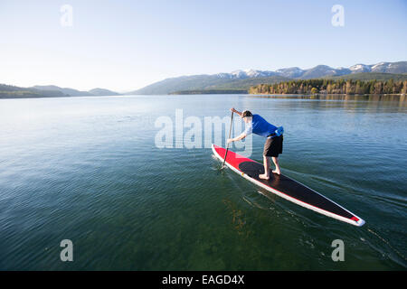 Ein Fit männlichen Stand up Paddle Boards (SUP) bei Sonnenuntergang am Whitefish Lake in Whitefish, Montana. Stockfoto