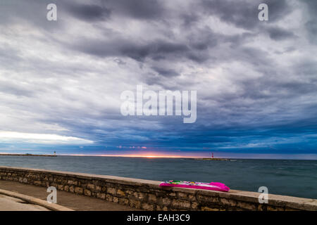 Sonnenuntergang auf der Luftmatratze auf Brüstung vor dem Mittelmeer mit roten Stahl Lookout und grünen oberen weißen Leuchtturm im bewölkten Hintergrund in der Nähe von Porec in Kroatien Stockfoto