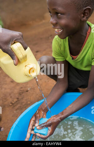 Ein Junge wäscht seine Hände mit Hilfe von einer Gemeinschaft Arbeiter - Bukwo District, Uganda, Ostafrika. Stockfoto