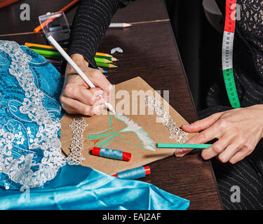 Mode-Designer zeichnet eine Skizze des zukünftigen Kleides auf Papier, neben Lüge Thread und Spitze Stockfoto