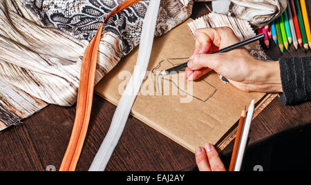 Mode-Designer zeichnet eine Skizze des zukünftigen Kleides auf Papier, neben Lüge Thread und Spitze Stockfoto